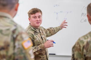 Student in Military Science writing on white board talking to others.