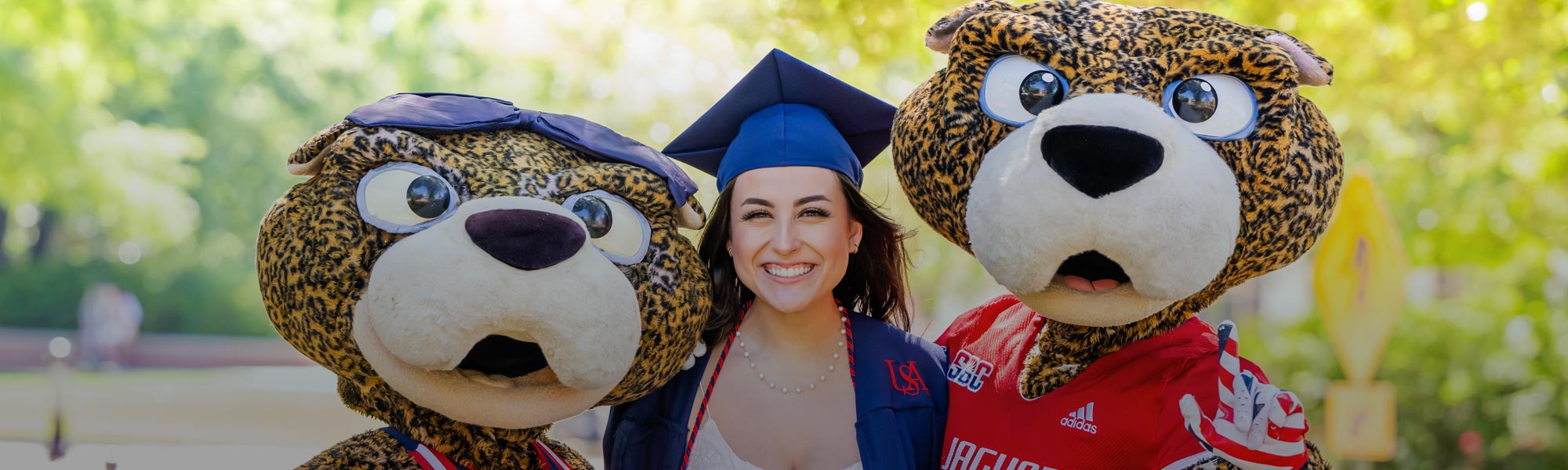 Female Student in cap and gown with SouthPaw and Miss Pawla