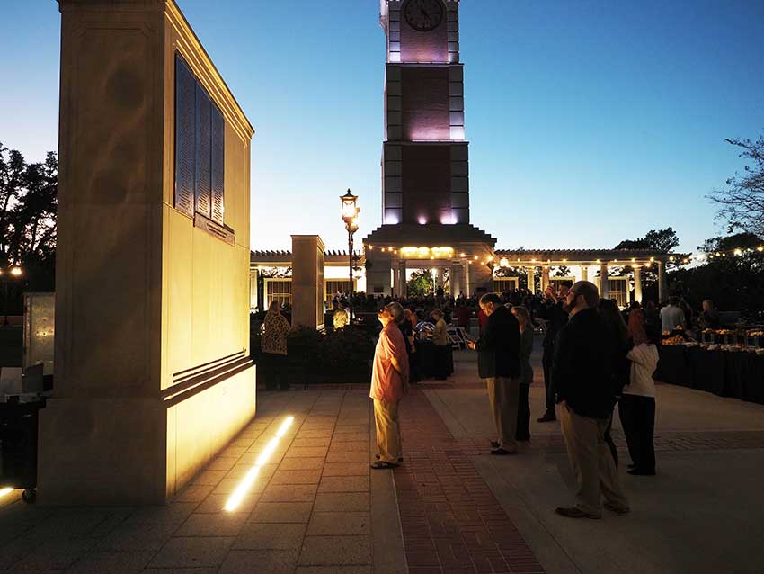 People looking at wall of honor at night with Moulton tower in background.