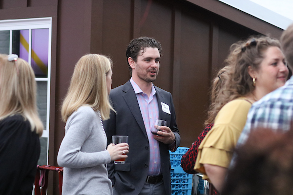 Man in pink shirt and jacket holding drink listening.