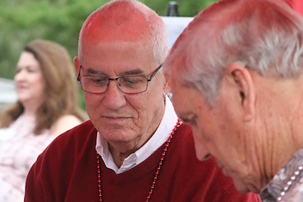 Two older men, one in red sweater, at event.