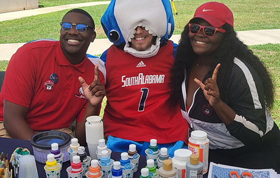 Student with shark head on with two other students painting at table.