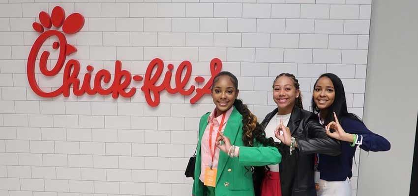 Three female students in front of Chick fil a sign.