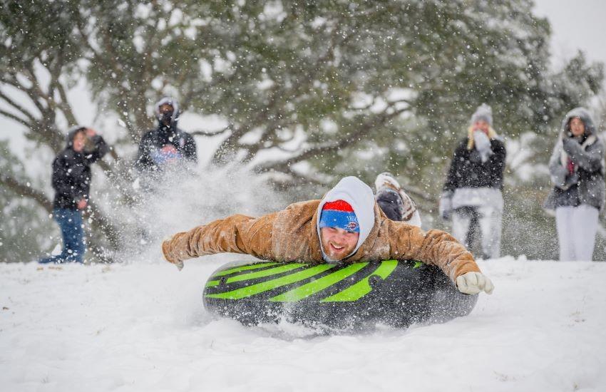 Student laying on tube sliding down hill with group watching. 