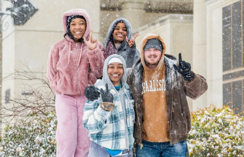 Students standing in snow holding up J hand.