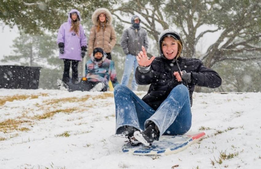 Student holding up J hand while sledding.