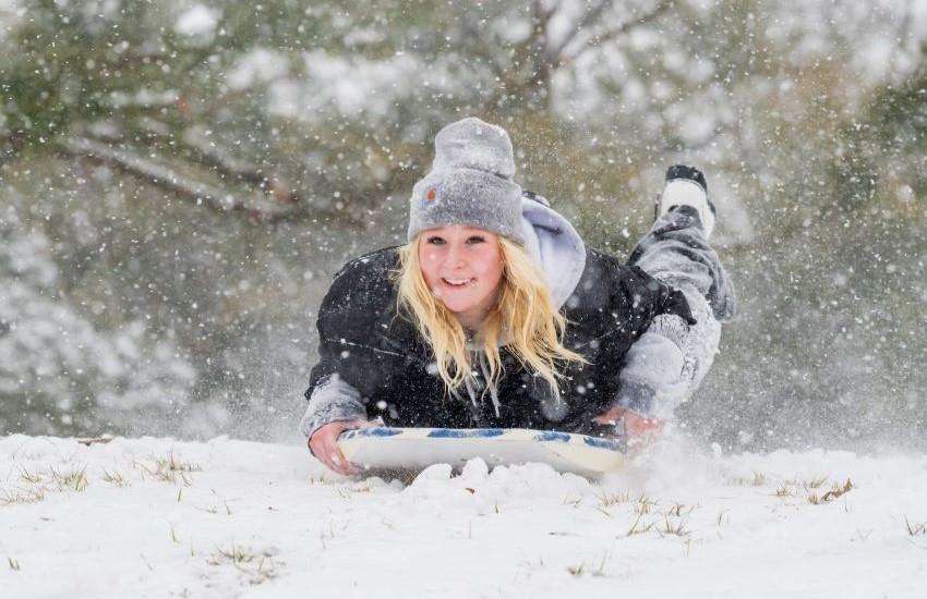 Student with beanie on sliding on snow.