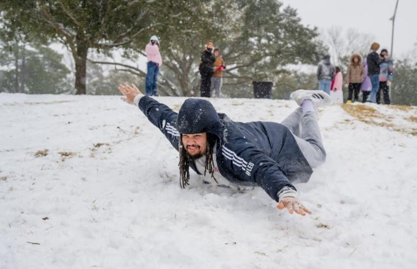 Student sliding down hill in snow on campus.