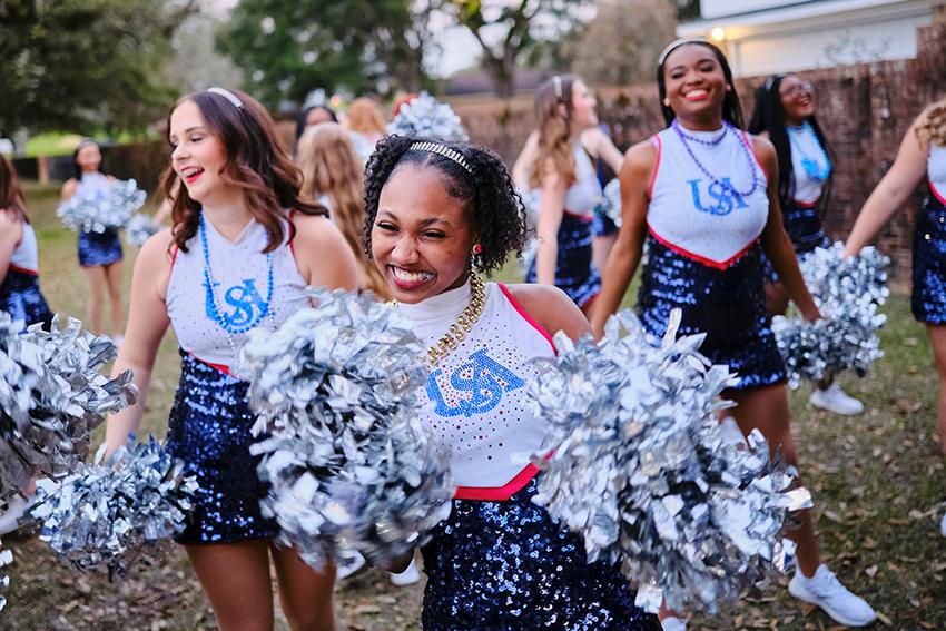 The cheerleader smiling with her pom poms during Mardi Gras Celebration