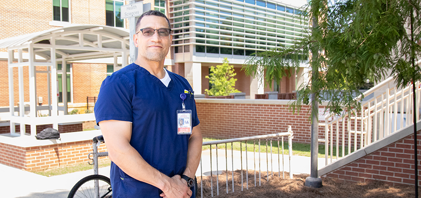 Miguel Negron in scrubs standing outside on campus.