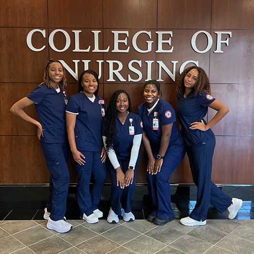 Mkali with other nursing students in uniform standing in front of the College of Nursing sign.