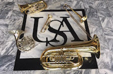 Pictured is the USA Logo on the marble floor of the Laidlaw Performing Arts Center Lobby.  Brass instruments are placed strategically and artistically around the logo.