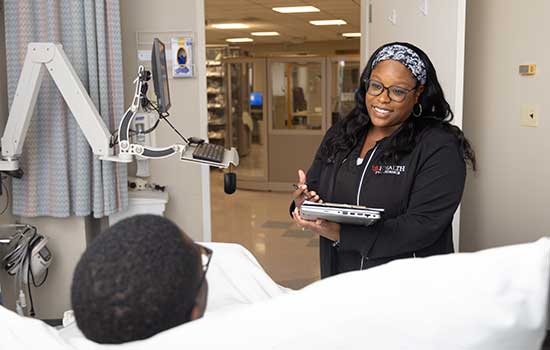 Nurse speaking with patient in hospital bed.