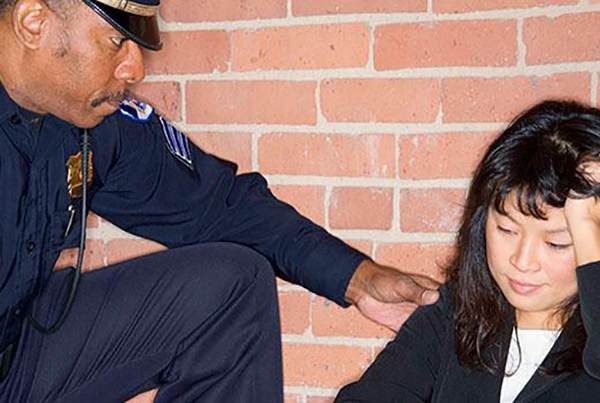 Policeman helping person sitting on ground who appears to be stressed.