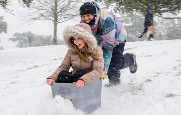 A student is pushed by another sledding down a hill in the snow. 