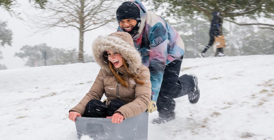 A student is pushed by another sledding down a hill in the snow. 