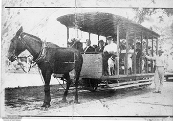 Black and white photo of a mule pulling a streetcar filled with passengers